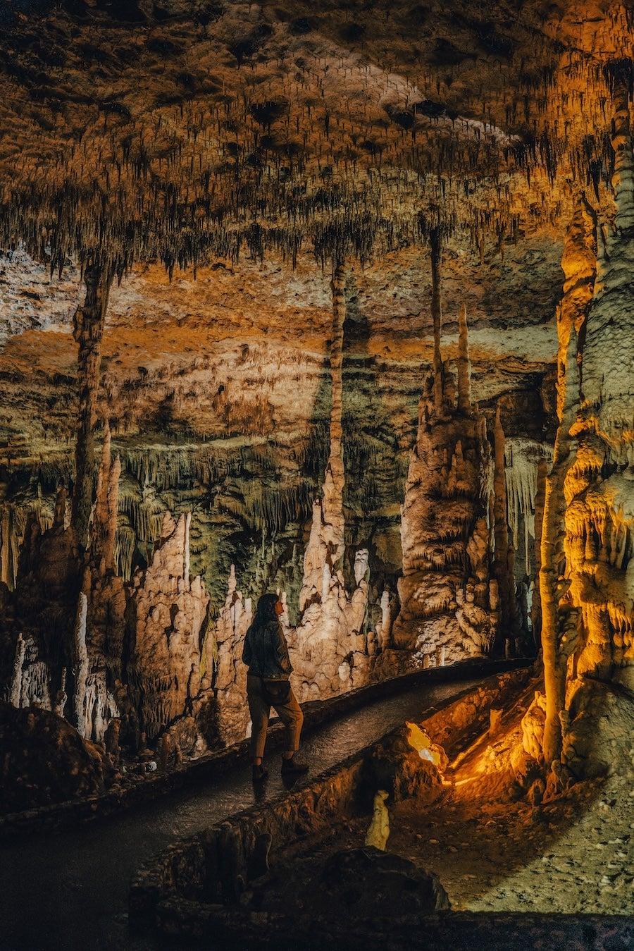 Cave interior with stalactites and a person walking along a dimly lit path.