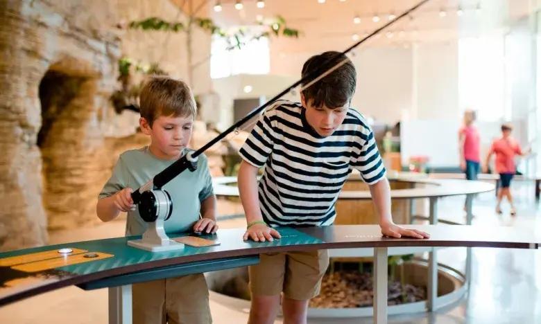 Two boys playing at an exhibit with a fishing rod indoors.
