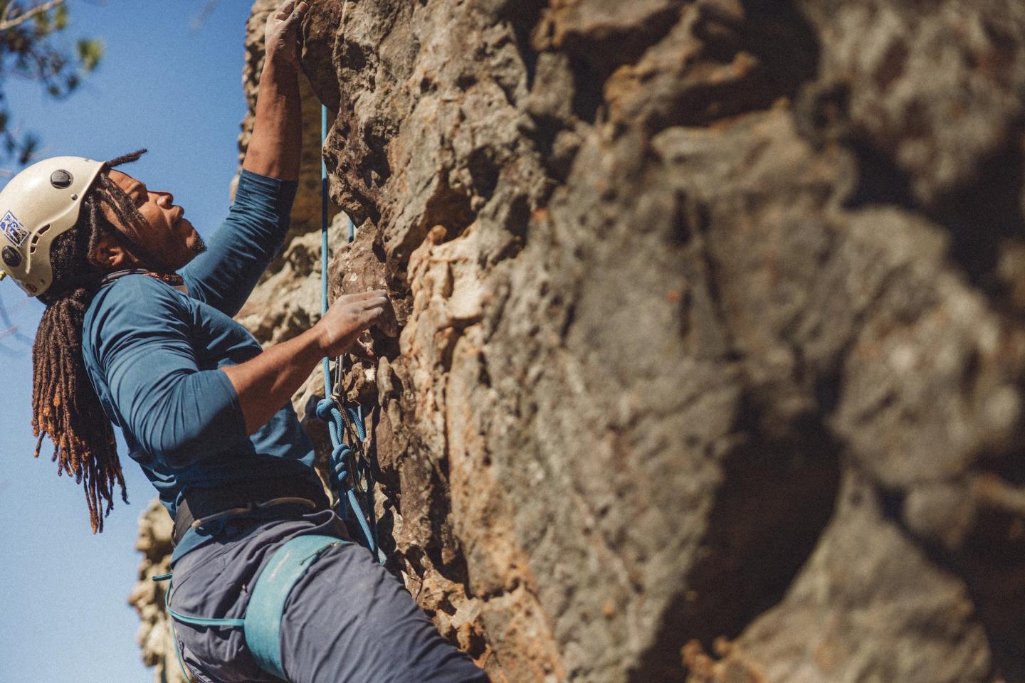 Rock climber ascending a cliff, wearing a helmet under a blue sky.