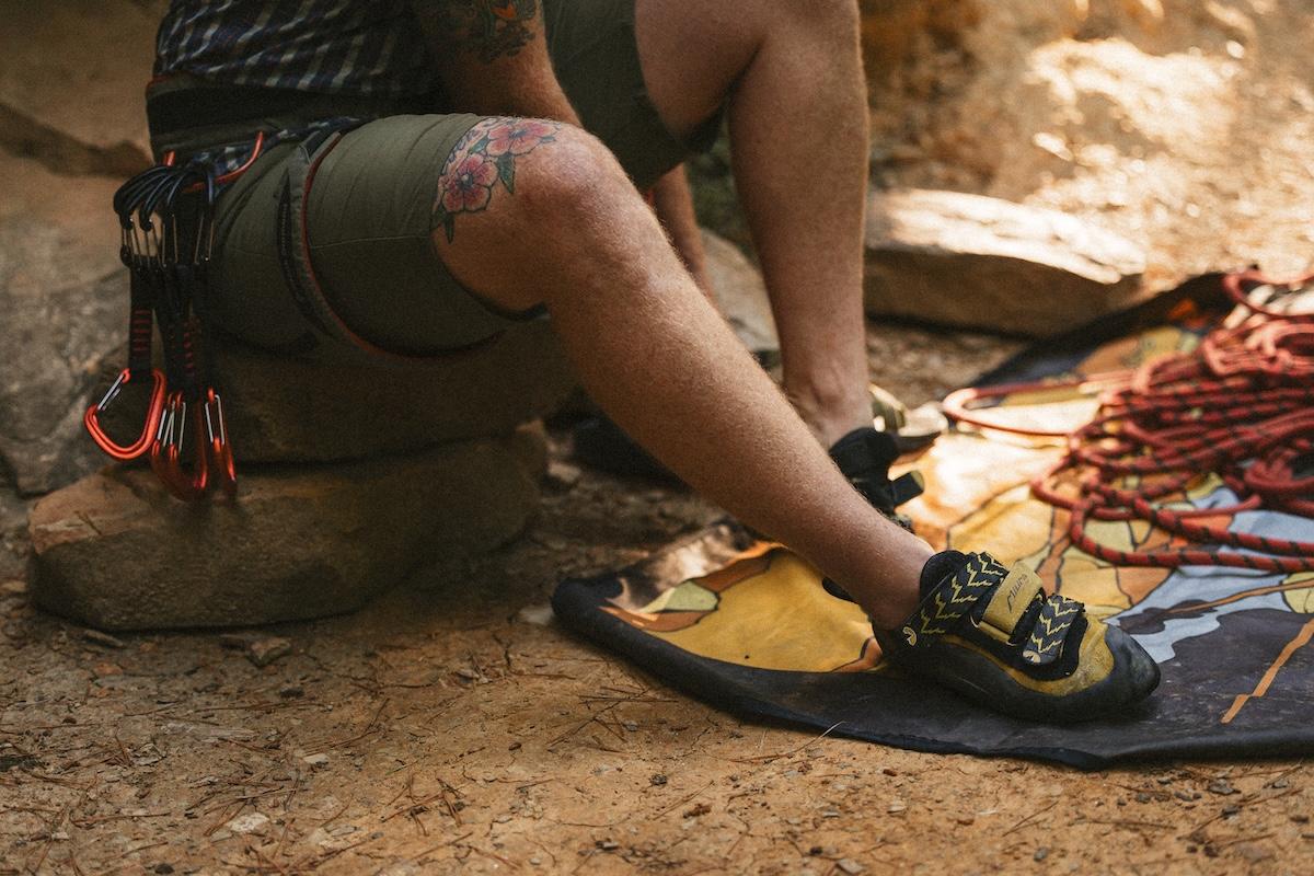 Rock climber sitting on ground with gear and ropes.