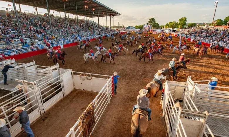 Crowded rodeo arena with horses, riders, and spectators in the stands.