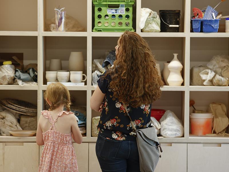 Woman and child looking at shelves with pottery and materials.