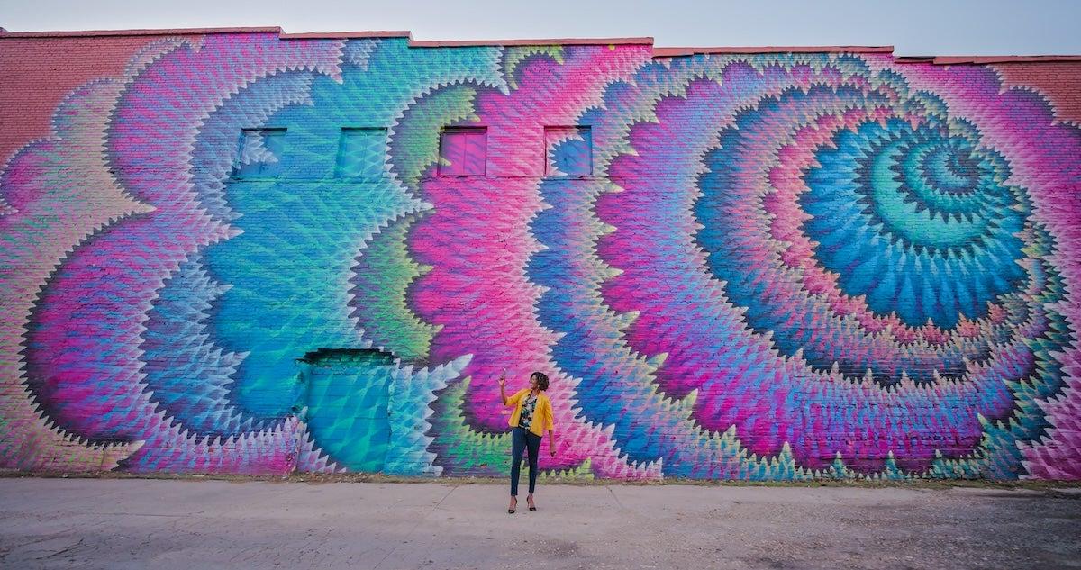 Colorful mural of swirling patterns with a person standing in front.